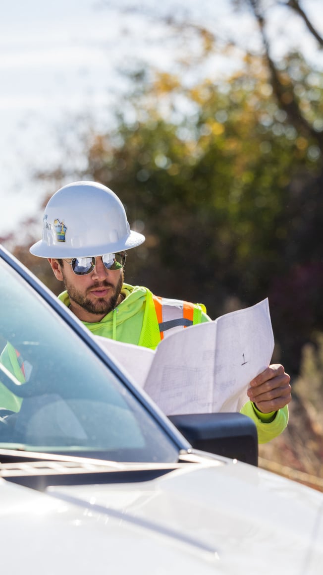 Leader on a renewable energy project in a white hard hat reading project plans next to a white work pickup