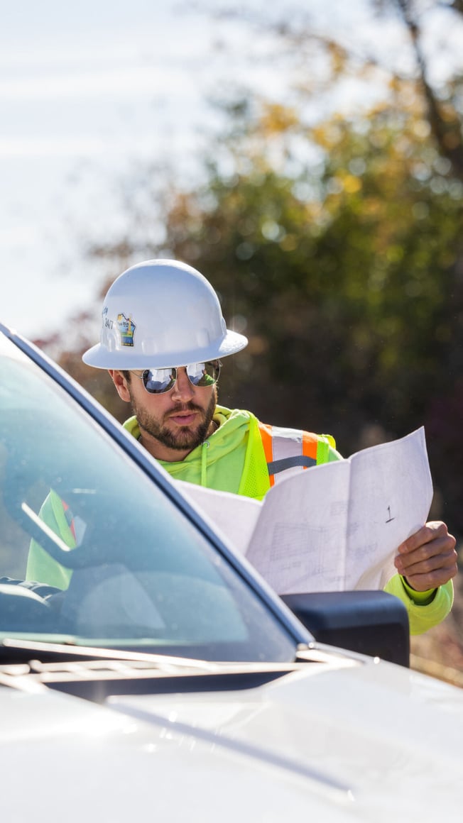 Caucasian male in field reviewing plans by a white work pickup truck