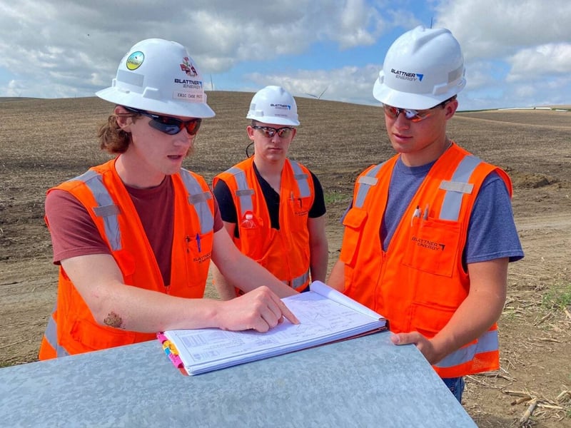 three field-based leaders reviewing paperwork on a wind energy project