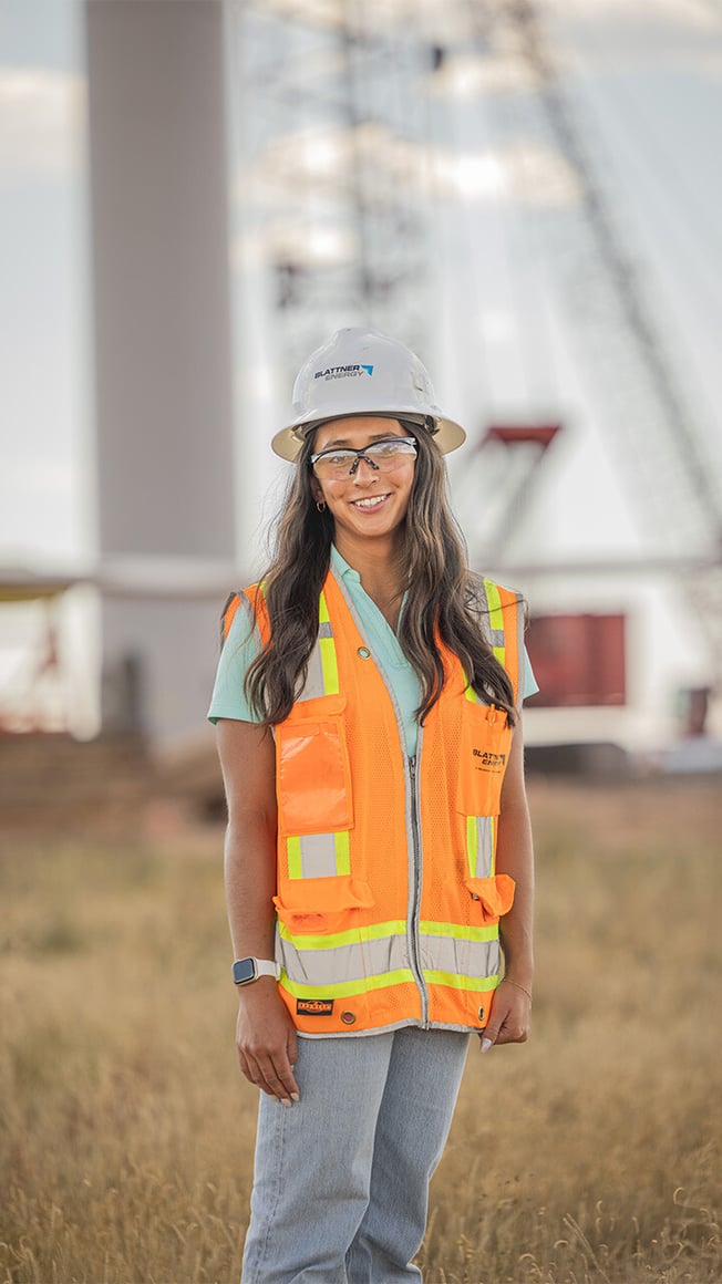 Female construction worker in foreground with wind turbine under construction in background