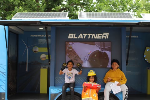 Three children pose in front of the community trailer during an education event.