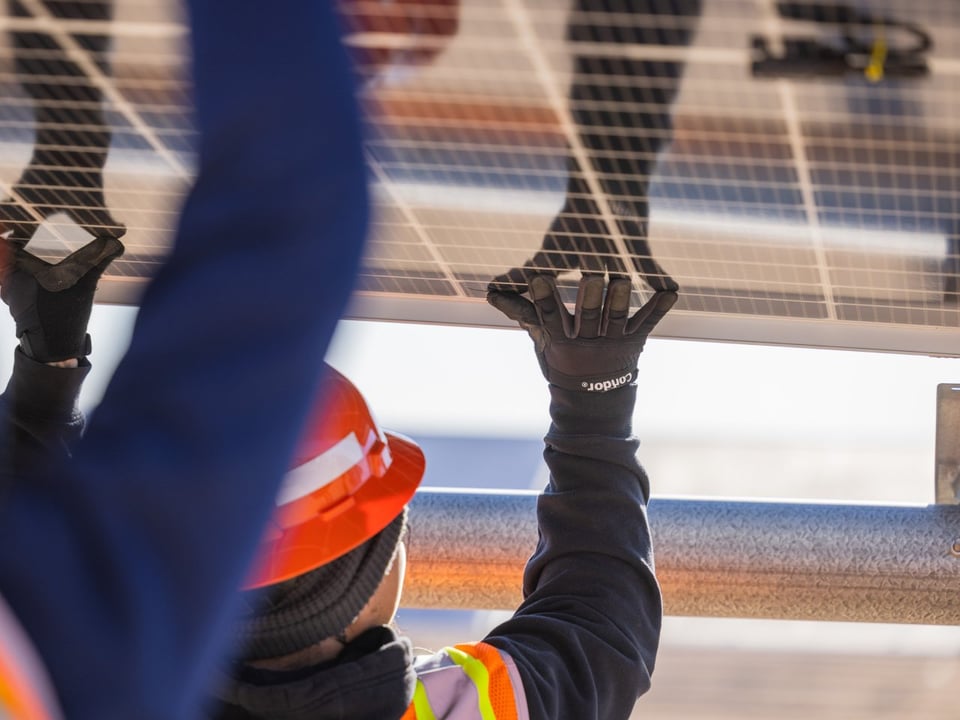 Close up of a field workers back while holding up a solar panel during install